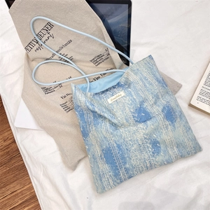 Detailed close-up of light blue tie-dye tote bag with lace pattern and fabric label