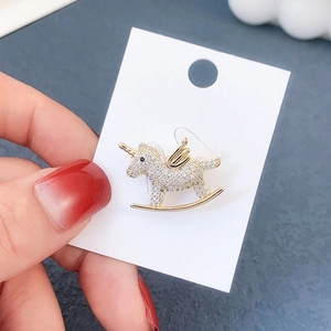Detailed close-up of a gold unicorn rocking horse brooch with white crystals