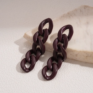 Macro detail of dark brown matte acrylic chain earrings on light marble texture