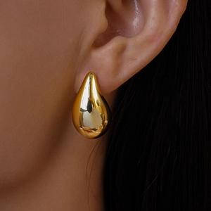 Close-up of a polished gold teardrop earring worn by a model with a glossy metallic finish