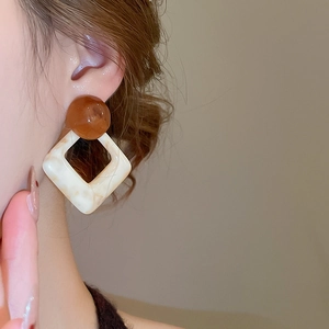 Detail of geometric resin earrings with amber bead and marble pattern square stud