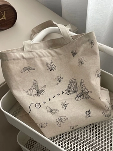 Detail view of canvas tote bag with butterfly prints and ZAKKA logo on a white metal cart