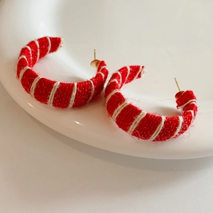 Detail of red fabric woven C-shaped hoop earrings with white stripes on a ceramic tray