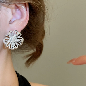 Makroaufnahme eines silbernen Blumenohrrings mit Zirkonia, getragen von einem Modell