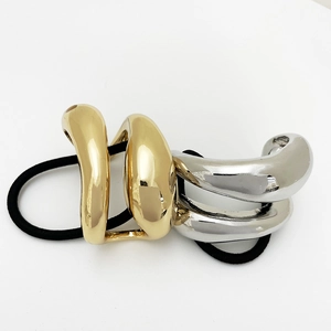 Close-up of sleek gold and silver curved metal ornaments on a black elastic hair tie