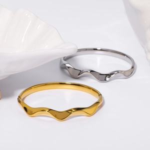 Polished stainless steel wave bangle in gold and silver finish on white background