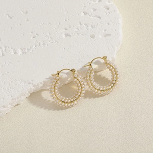 Detailed close-up of gold hoop earrings encrusted with small white pearls on stone
