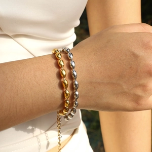 Close-up of gold and silver stainless steel oval bead bracelets on a model's wrist