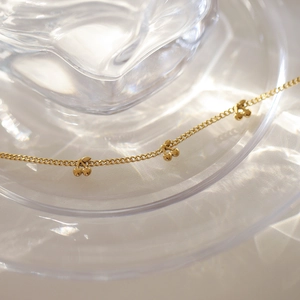 Detail of gold cherry pendant necklace on wavy glass with water ripple shadows