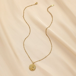 Detail of a gold coin necklace featuring an engraved crane design on a delicate bead chain