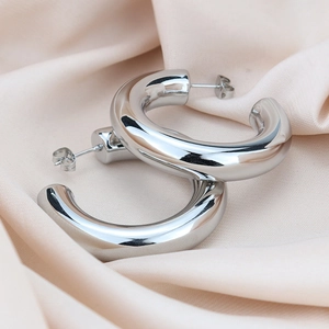 Polished silver chunky C-shaped hoop earrings on elegant champagne silk fabric background