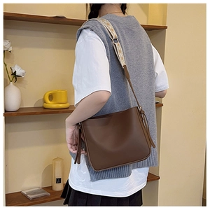 Chic brown leather crossbody bucket bag featuring a trendy patterned wide shoulder strap