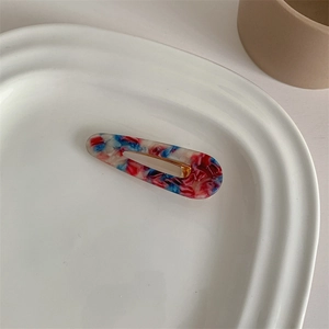 Close-up of marble patterned acetate hair clip with gold metal base in a ceramic tray
