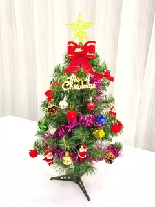 Close-up of mini green Christmas tree with golden star, red bows, and colorful ornaments