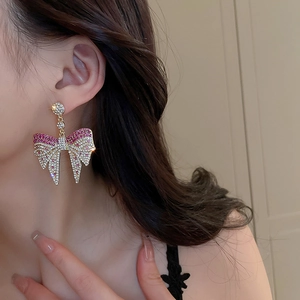Detail of bow-shaped golden earrings with pink crystals worn by a model