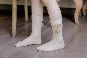 Detail of cream ribbed knee-high baby socks with cute cherry-shaped pom-pom bow decor