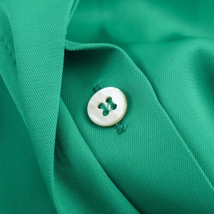 Detailed close-up of a bright green satin shirt with a white four-hole button and smooth texture