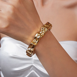 Close-up of a wide golden irregular textured cuff bracelet on a female wrist