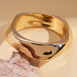 Close-up of a wide golden wave textured cuff bracelet on a natural stone display