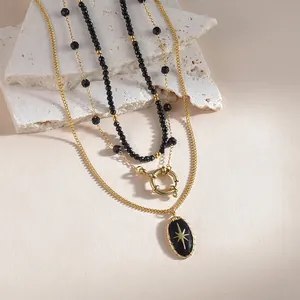 Three-layer gold necklace with black beads and oval starburst pendant on a stone background