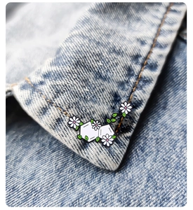 Close-up of a white flower and green leaf enamel pin on a denim jacket collar