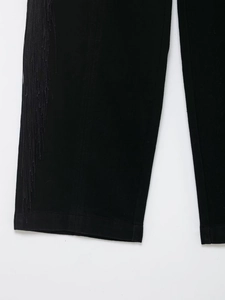 Gros plan détaillé des longues franges noires sur la couture latérale du pantalon en coton