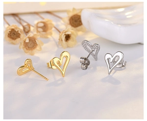 Detailed view of hollow heart stud earrings in gold and silver on a ceramic tray