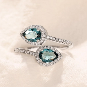 Close-up of bypass ring featuring dual pear-cut blue stones with pave diamond accents