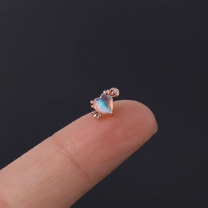 Macro view of tiny heart-shaped opal stud earring in rose gold on a fingertip