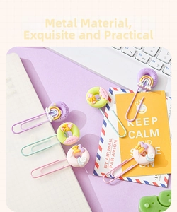 Close-up of macaron metal paper clips with rainbow and donut charms on a notepad