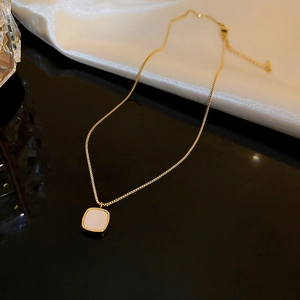 Detail of gold box chain necklace with square shell pendant on white silk fabric