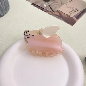 Close-up of a pink acetate pig-shaped hair claw clip with white wings on a white plate