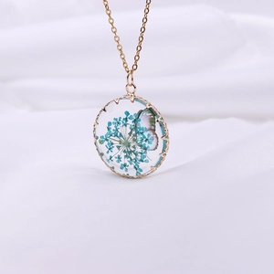 Detail of round gold pendant with blue dried flowers and butterfly in resin
