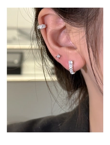 Close-up of stacked silver U-shaped earrings and star studs set with clear zircon stones