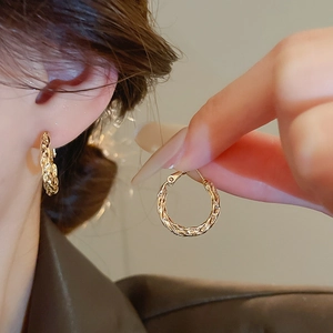 Close-up of elegant gold twisted hoop earrings showing refined metal texture on a model