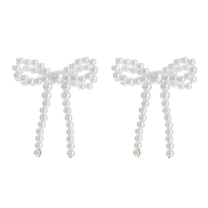 Close-up of elegant white faux pearl earrings with golden bow design on white background