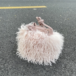 Close-up of pink faux fur bucket bag featuring a leather drawstring on asphalt