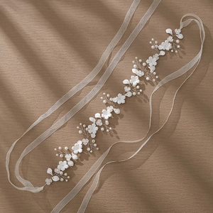 Handmade bridal headband with white ceramic flowers, pearls and long ribbons on a wood surface