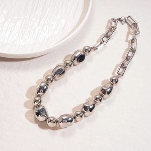 Chunky silver metallic necklace with irregular beads and polished links on beige surface