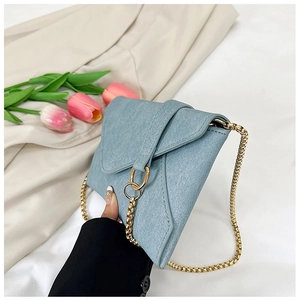 Detail of light blue denim envelope crossbody bag with gold ring and chain strap