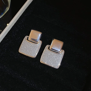 Macro detail of geometric silver square stud earrings with shimmering glitter texture