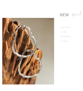 Detail of silver wavy hoop earrings with polished texture on a natural wooden stand