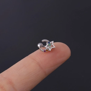 Macro view of tiny star and crescent moon ear stud with colorful crystals on fingertip