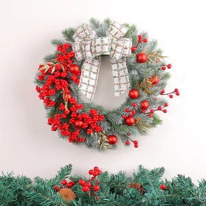 Christmas wreath with red berries, pine needles, and a plaid bow on a white wall