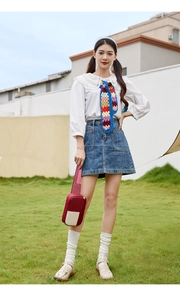 Outdoor shot of woman wearing crochet necktie and holding red and white shoulder bag
