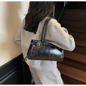 Polished black leather rectangular shoulder bag with gold hardware shown on a model