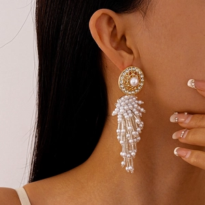 Gros plan de boucles d'oreilles dorées à pampilles avec perles et strass sur modèle