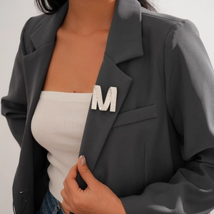 Detailed view of luxury silver M-letter brooch with rhinestones on a blazer lapel