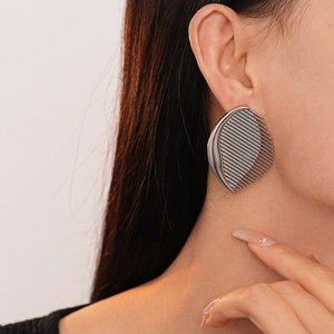 Macro detail of metallic fan-shaped earring with textured stripe pattern and silver finish