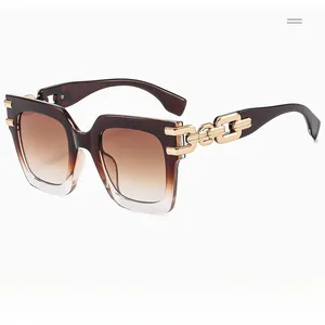 Detail of square oversized sunglasses with brown gradient lenses and gold chain temples